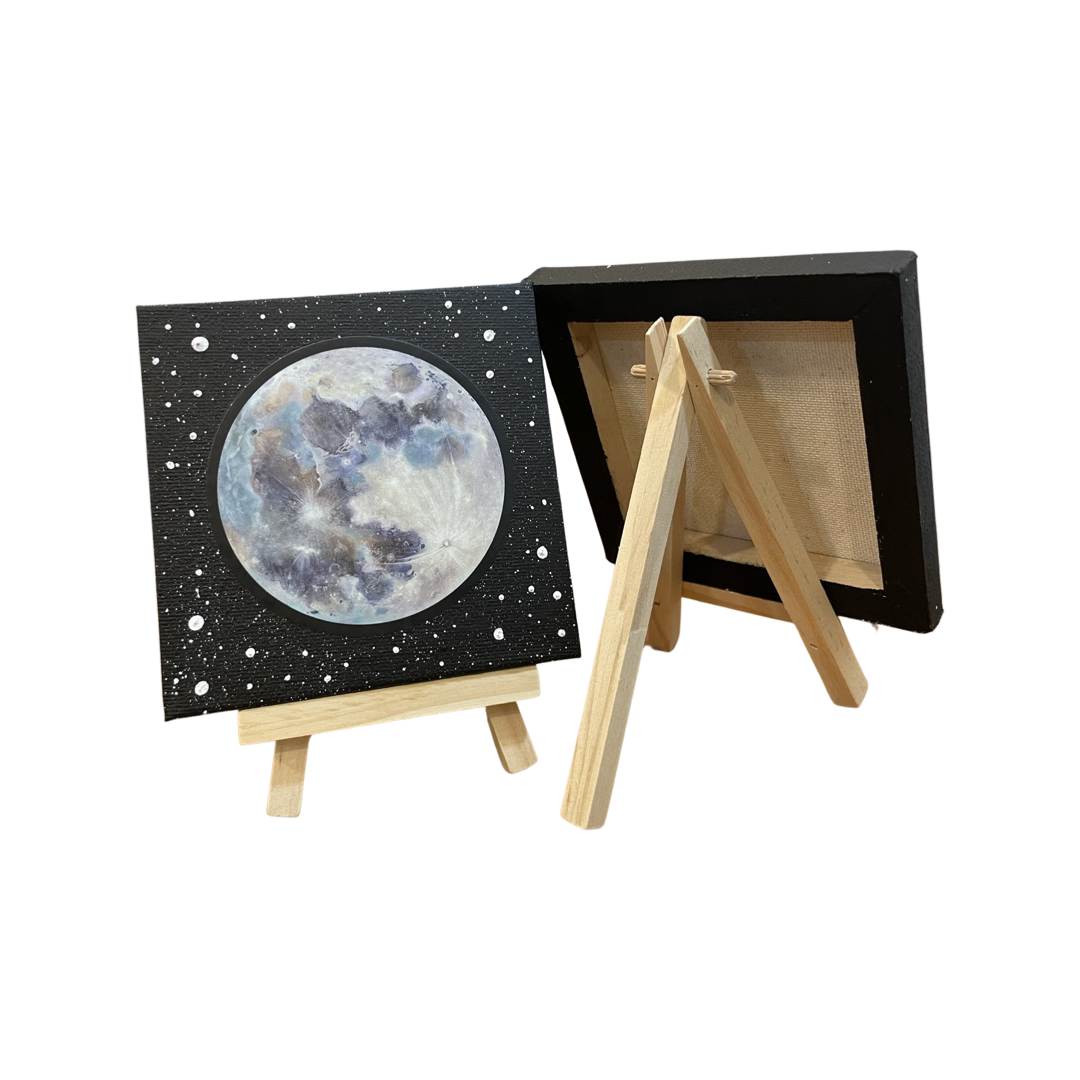 Four by four inch canvas on a natural wood stand. Painting depicts full moon against a black background with the impression of stars. The full moon is a vinyl sticker reproduction of an Elizabeth Schnura original painting, Magnolia's Moon, created in 2022.